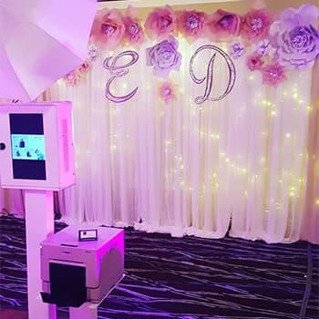 An image of our classic printing photo booth with a custom paper flower wall photo booth backdrop